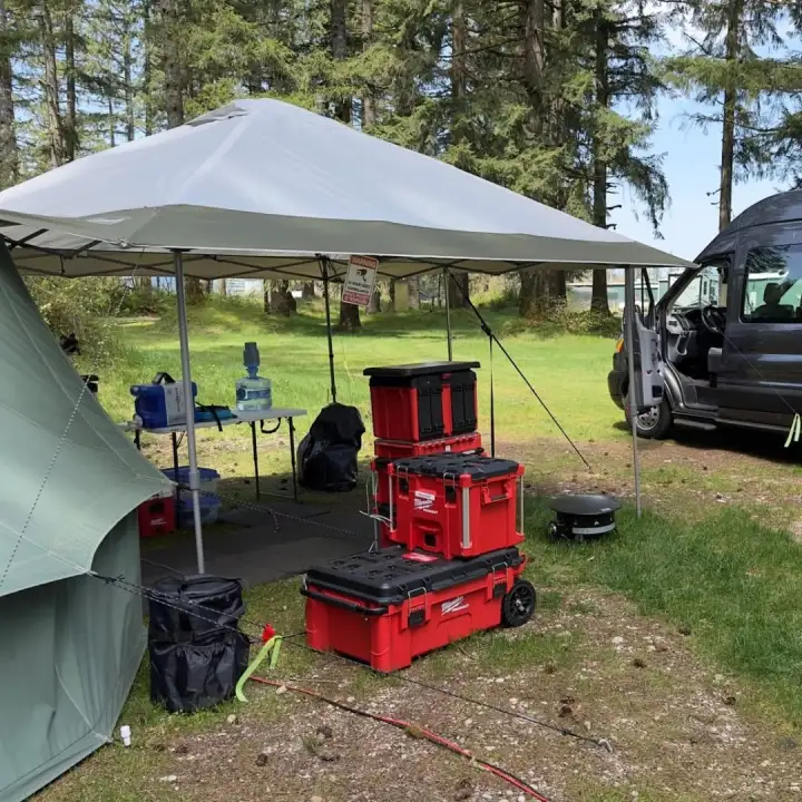 A camp setup with the van, a tent, and gear under a shade canopy.